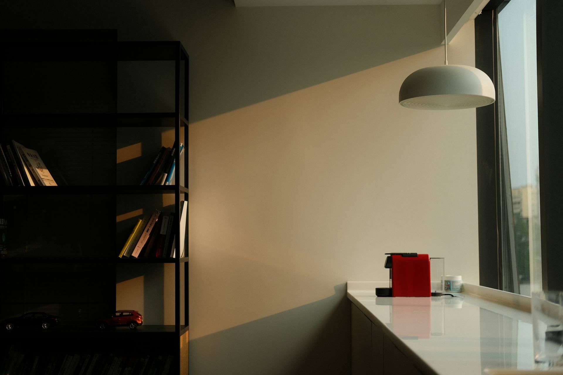 A quiet office with a bookshelf and pendant lamp beside a tall window